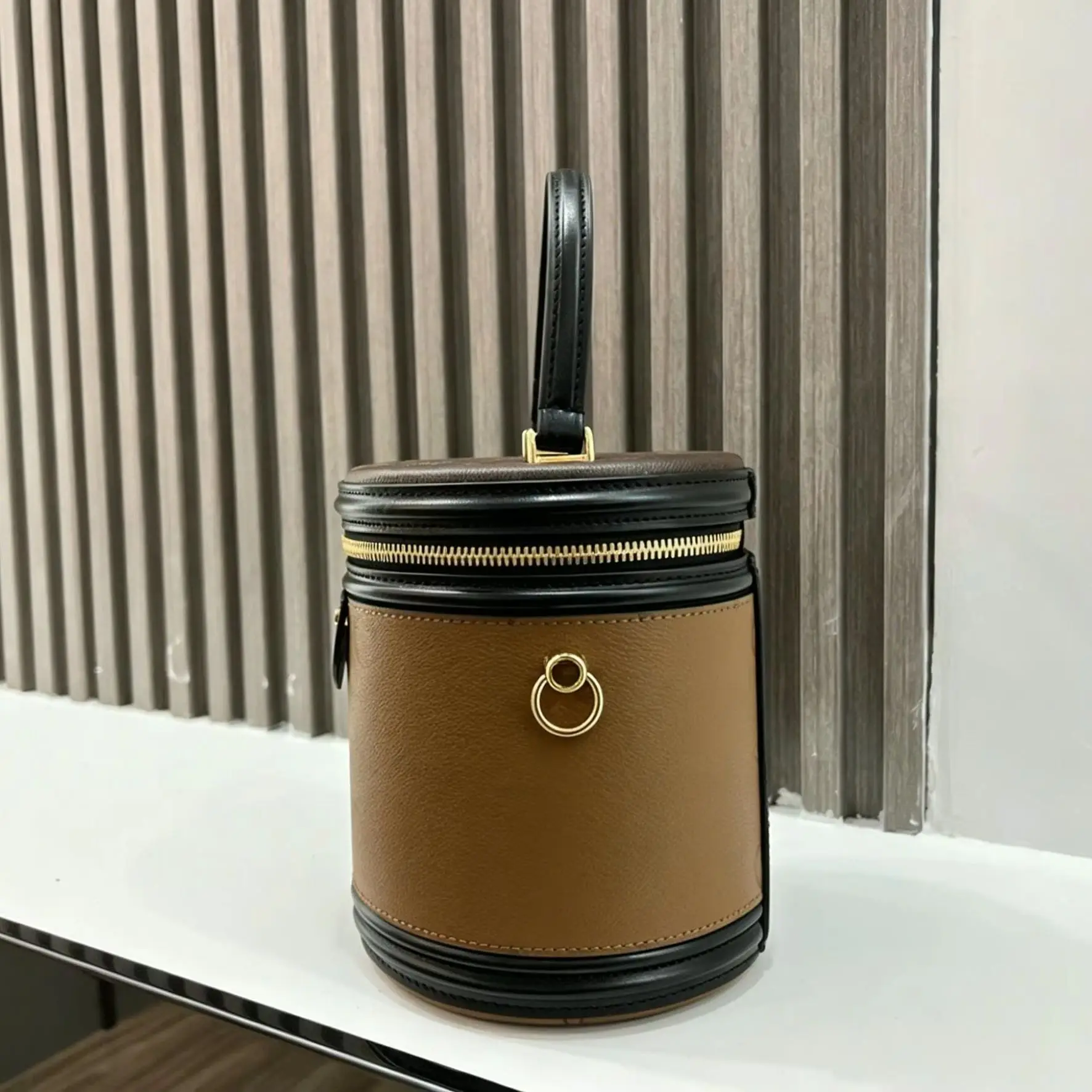 Bolso de mano cilíndrico de cuero granulado color marrón camel con detalles en negro, asa superior, cierre de cremallera dorada, hebilla de anillo metálico, estilo retro, para mujer, tipo bandolera.