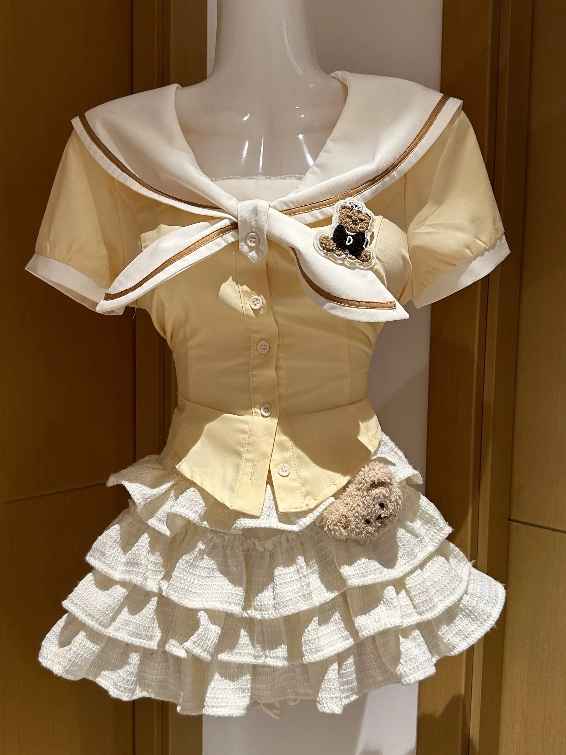 

Милый школьный комплект из двух предметов: темно-синяя рубашка с воротником и завязками на талии, а также белая многоярусная юбка из полиэстера с коротким рукавом на пуговицах.