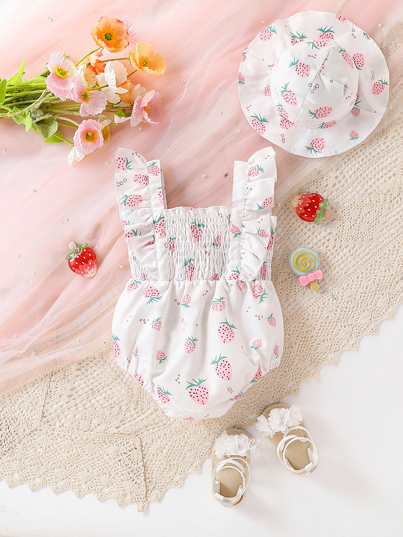 Cute baby girl in a casual romper with a strawberry pattern all over, including a hat accessory, for summer.