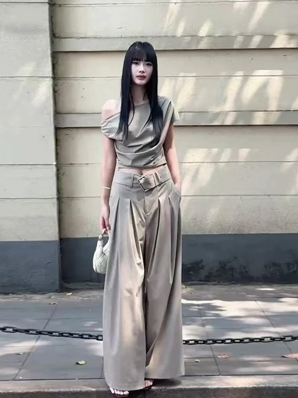 

Комплект: брюки с высокой талией и широкими штанинами, асимметричный топ на одно плечо с драпировкой и брюки. Модный летний женский ансамбль 2025 года.