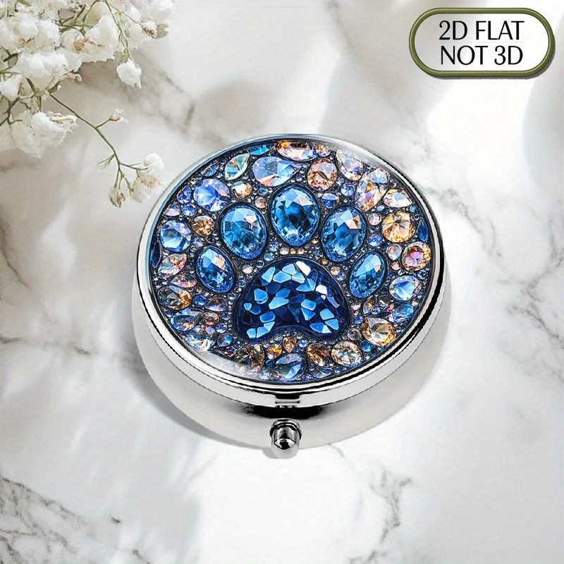 A flat, portable, round metal pill box, adorned with a shiny crystal paw print and surrounded by colorful gemstones, designed for the organized storage of medication. It is ideal for storing vitamins and small accessories, making it a perfect travel gift for relatives, friends, or elders. Flat design