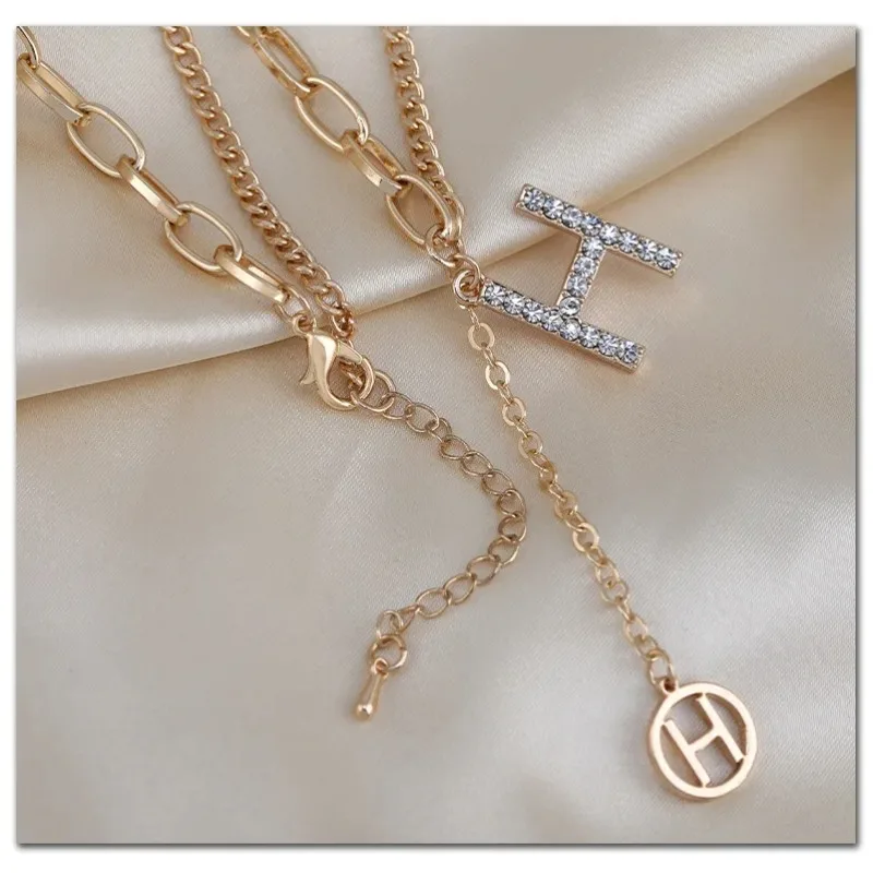 

This fashionable and versatile piece features a short sweater, a necklace with the letter "H" and tassels