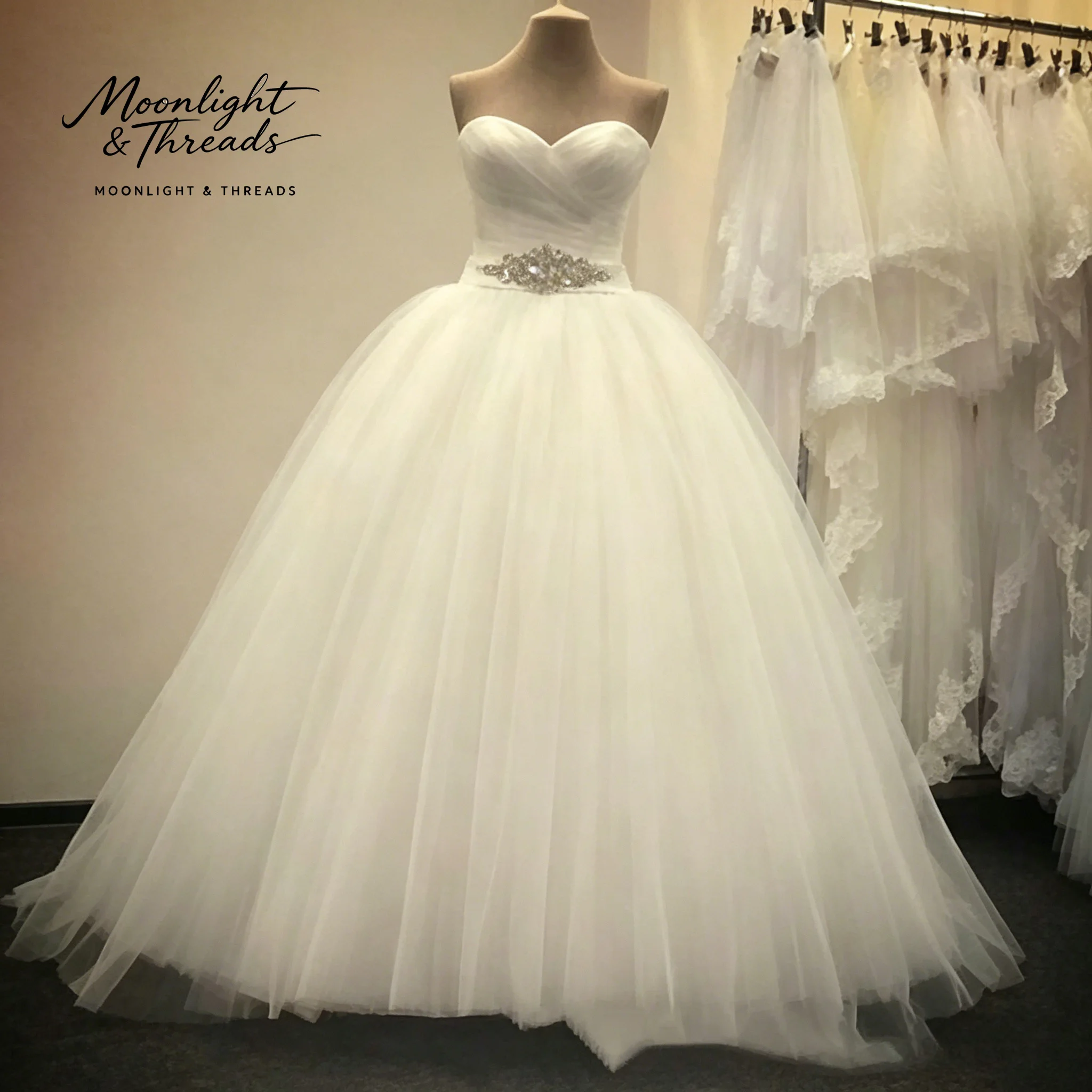 

White strapless sleeveless floor-length formal wedding gown with a full skirt draped waist and crystal pendant