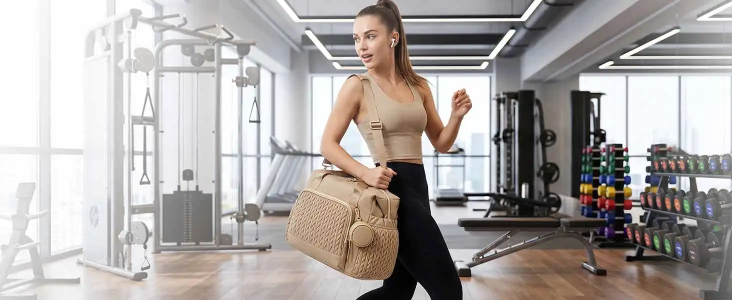Woman in white sports bra and tan/beige shorts holding resistance band, standing in bright modern gym with equipment visible in background.