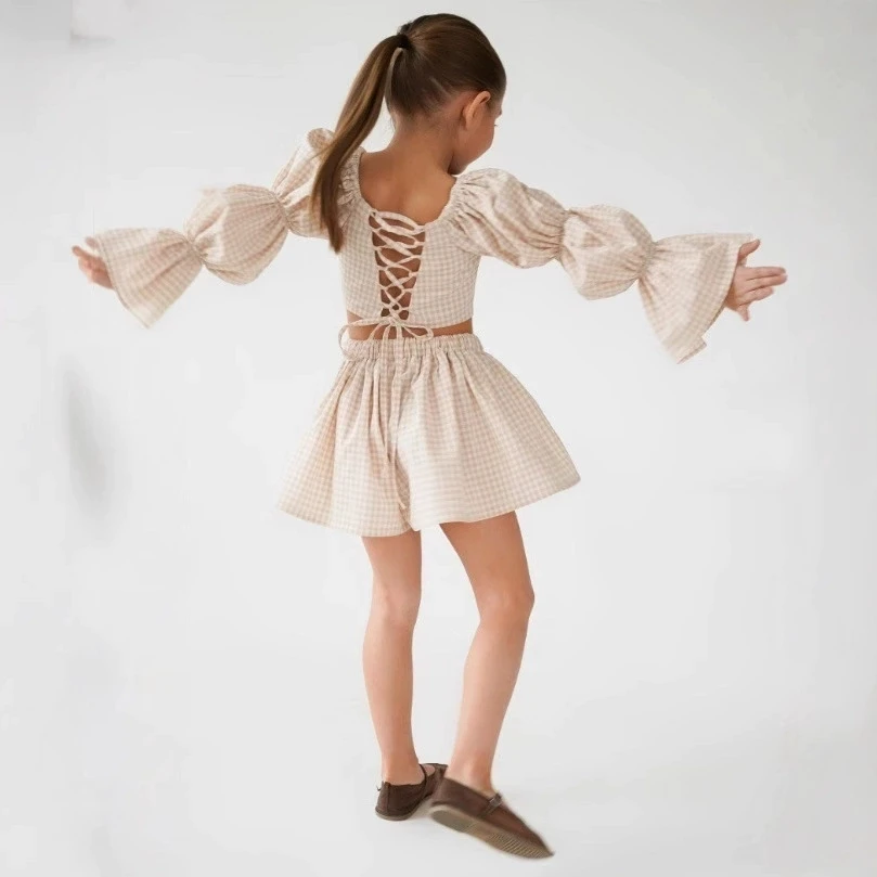 

Детский комплект из двух предметов: топ с французским клетчатым узором и асимметричной шнуровкой, и повседневные шорты. Коллекция Весна-Осень 2025.