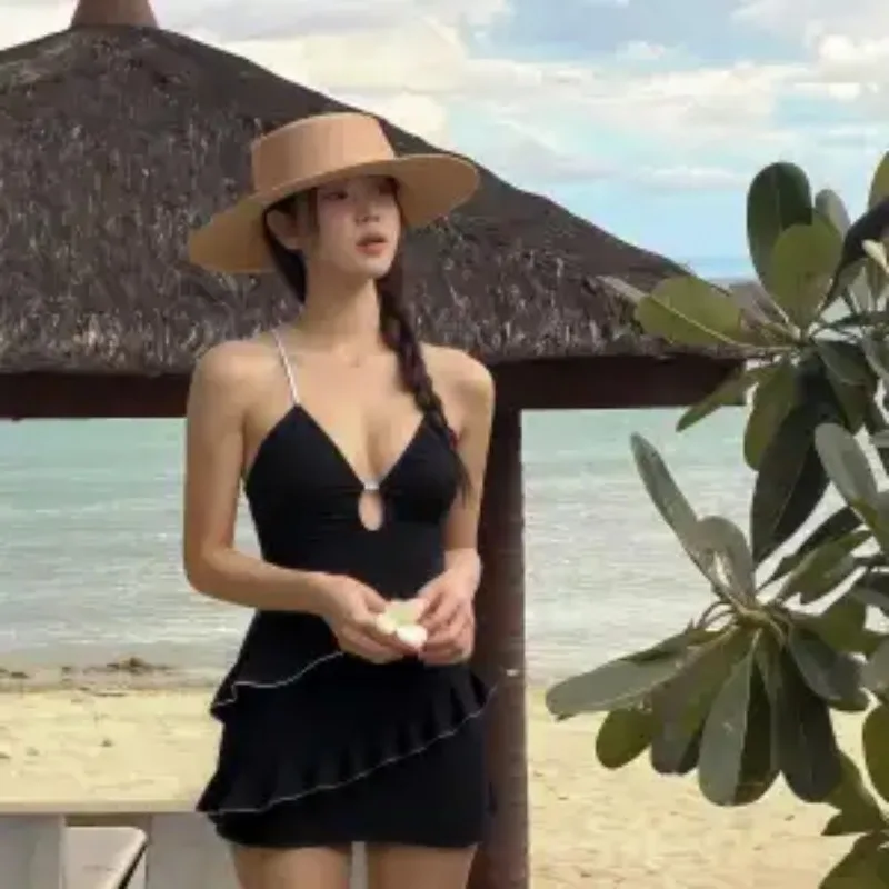 

Женское черное цельное купальное платье с завязками на спине и рюшами по подолу юбки