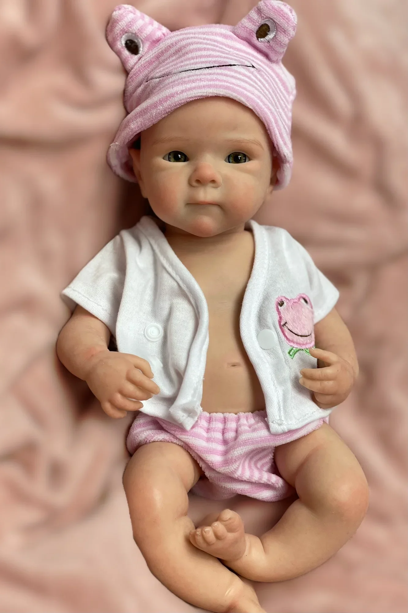 

New 13 inch full body silicone bettie girl cute reborned doll, with bald head and pink frog clothes. Is a good gift for kids.