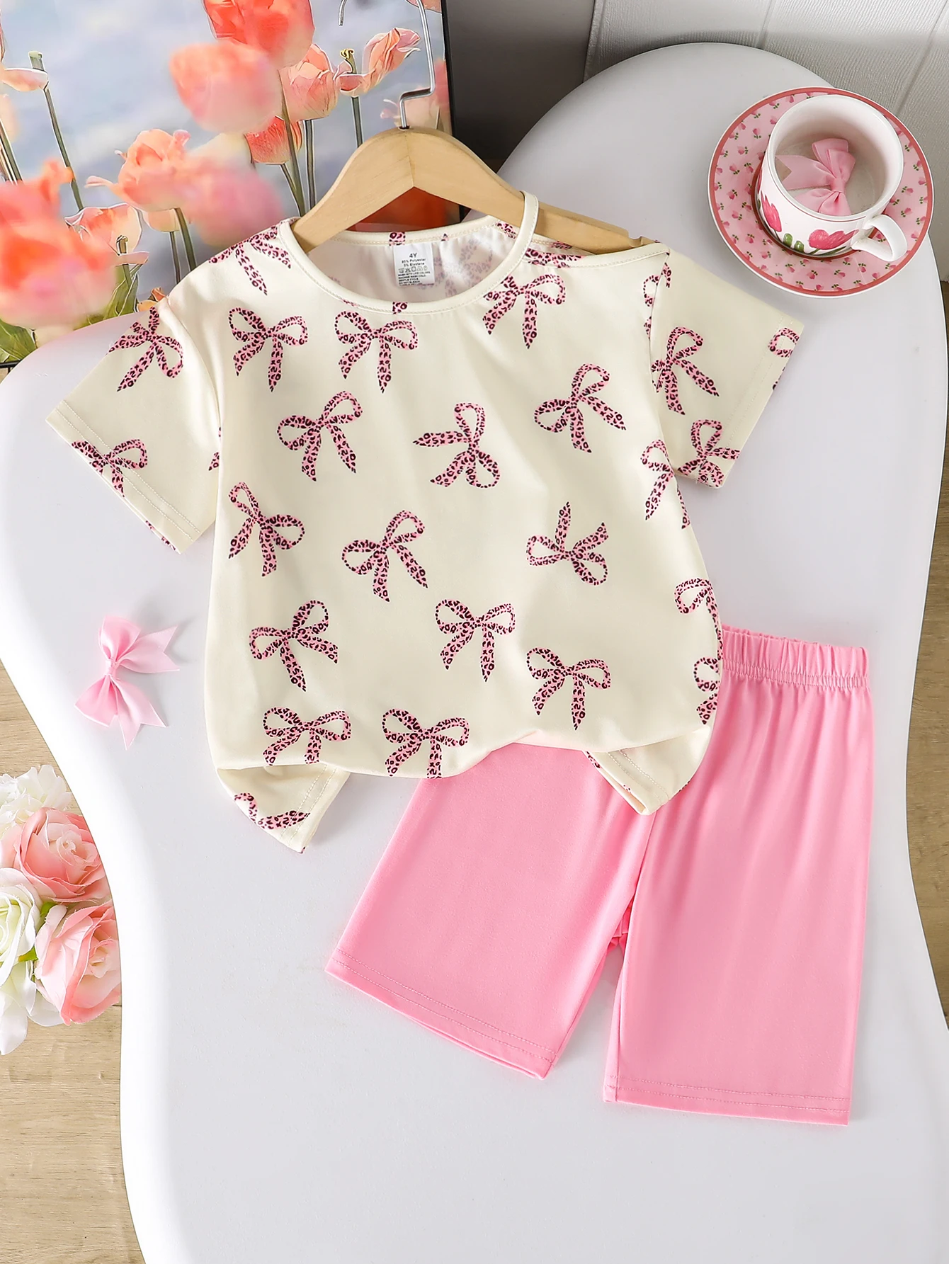 New 2-Piece Set for Girls: Summer Thin Shorts Outfit, Children's Comfortable Soft Bow Print Round Neck Asymmetrical Shoulder Strap Hollow-Out Pullover Top + Solid Color Elastic Waist Shorts Two-Piece Set. Cute and Fashionable Girl's Clothing, Youthful Sweet Princess Vacation Style Outfit for Girls Aged 4-5-6-7-8 Years. Suitable for Outdoor Activities, Casual Wear, Parties, Festivals, Eid, Easter, and Carnival for Girls