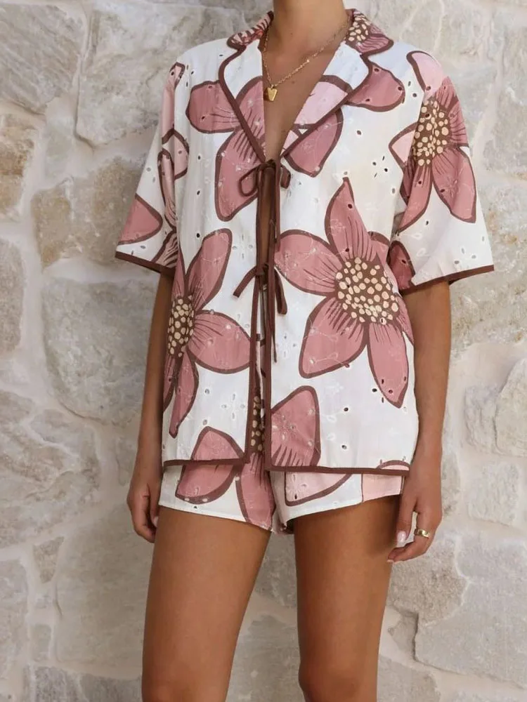 

Повседневный комплект из двух предметов: свободная рубашка с коротким рукавом и воротником-стойкой на шнуровке, а также брюки. Модный женский костюм 2026 года с элегантным цветочным принтом и ажурными вставками.