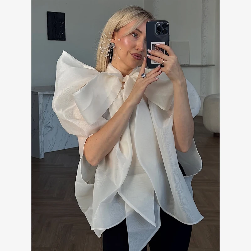 Biała szyfonowa bluzka z dużym wiązaniem, stójką, rękawami typu cape, nieregularnym drapowanym dołem, luksusowa, elegancka, w stylu socjality, na imprezę, codzienna.