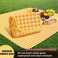 Yellow gingham waterproof picnic mat folded on grass with fruit and picnic snacks