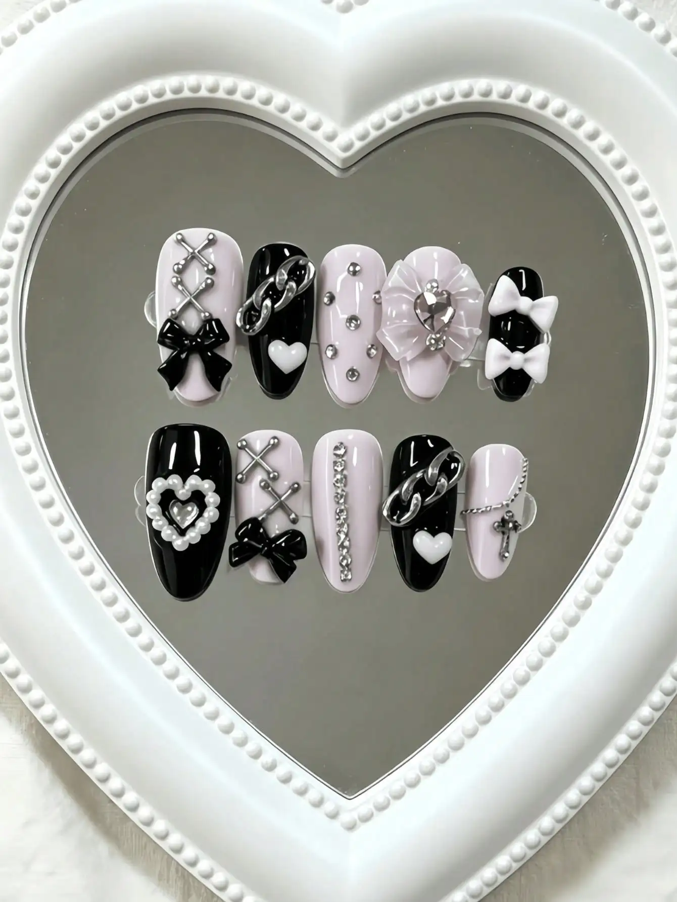 10 faux ongles en forme d'amande, de longueur moyenne, noirs et roses contrastés, dans un style subculture doux et cool, avec des chaînes métalliques, des nœuds 3D et des strass en forme de cœur, avec des couleurs contrastées noires et roses et des techniques de décoration métallique, adaptés aux filles stylées et aux femmes branchées, parfaits pour les festivals de musique, les sorties en ville et les soirées branchées, livrés avec de la colle gelée et une lime à ongles.