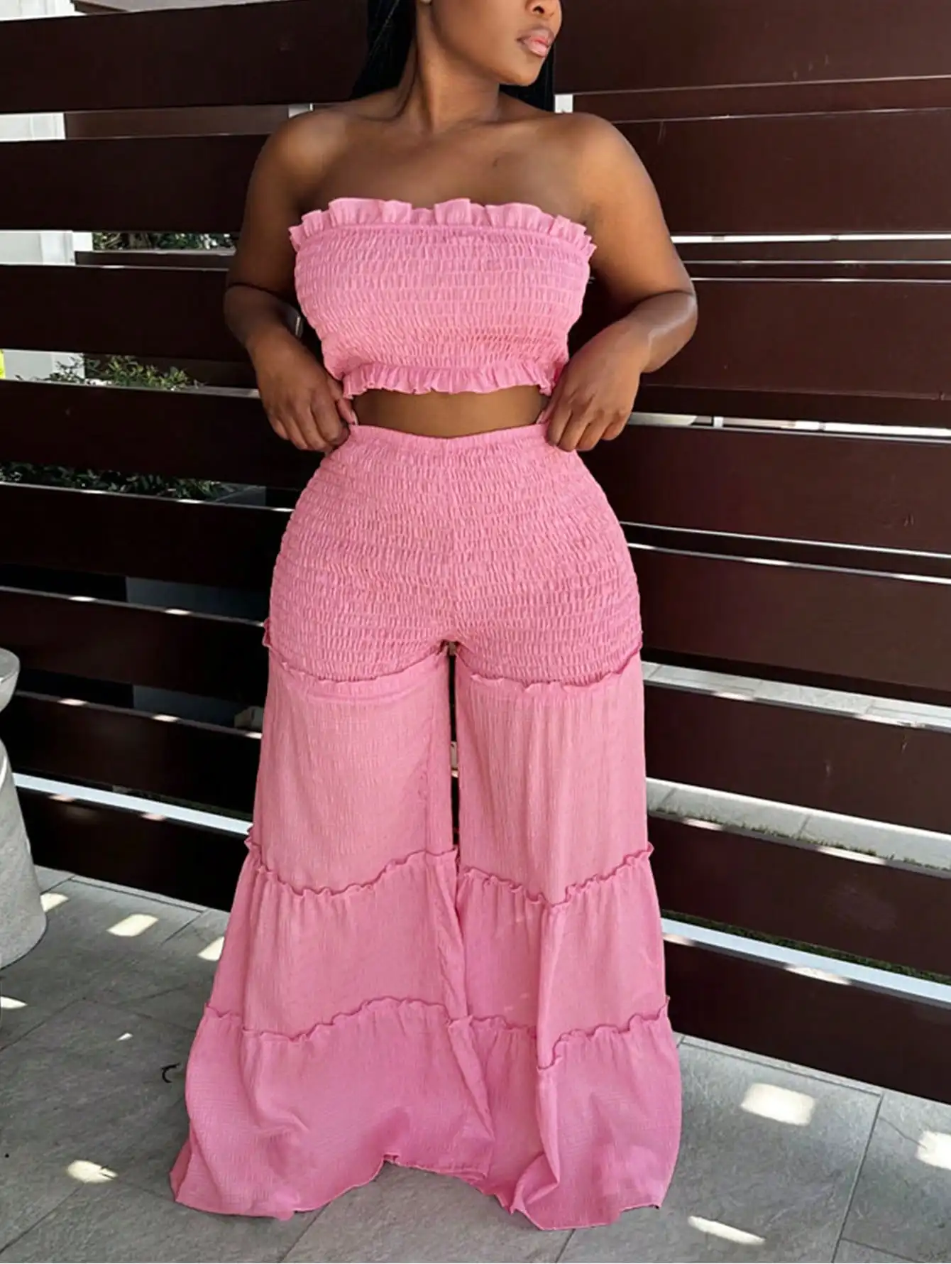 

Розовый комплект из топа-бандо с рюшами и широких брюк с многоярусными оборками для пляжного отдыха