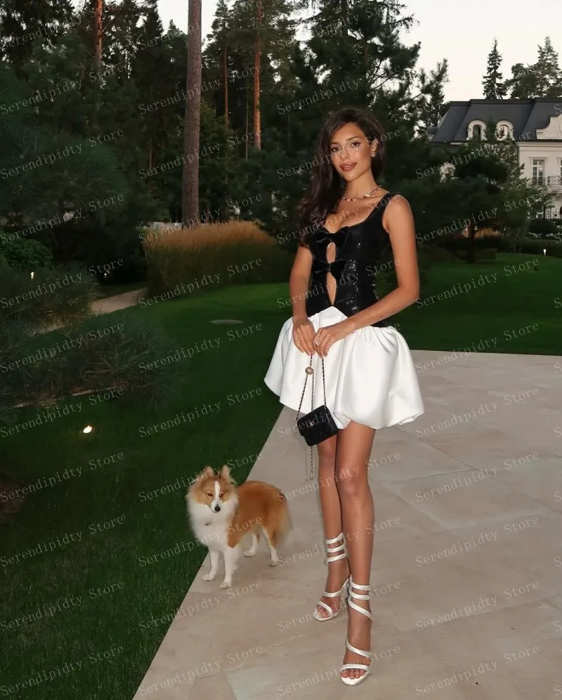 Haut à paillettes noir poli avec grand nœud et jupe en satin blanc, design ajusté révèle le ventre associé à un sac à sangle en chaîne