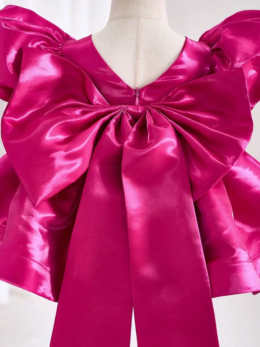 Vestido de noche de satén fucsia con lazo gigante en la espalda y mangas abullonadas