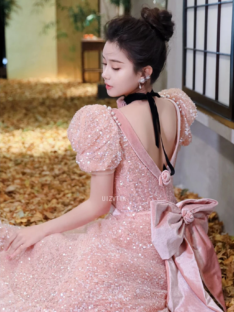 ชุดราตรีสีชมพู แขนพองสั้น คอวี ประดับเลื่อม แต่งโบว์ พร้อมระบายชายกระโปรงยาวลากพื้น สำหรับงานพรอมหรืองานเลี้ยงอย่างเป็นทางการ