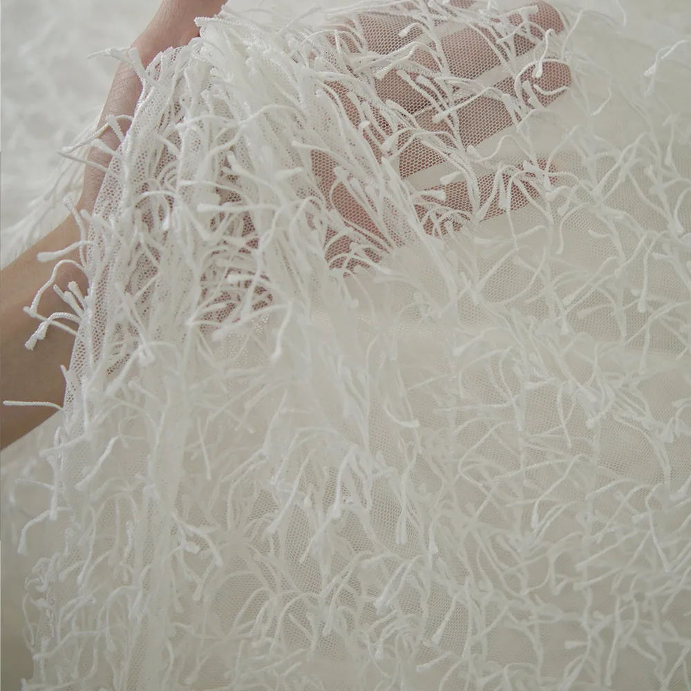 Weißer Spitzenstoff mit Fransen und der strukturierte, netzähnliche Stoff für Hochzeitskleider und formelle Kleider