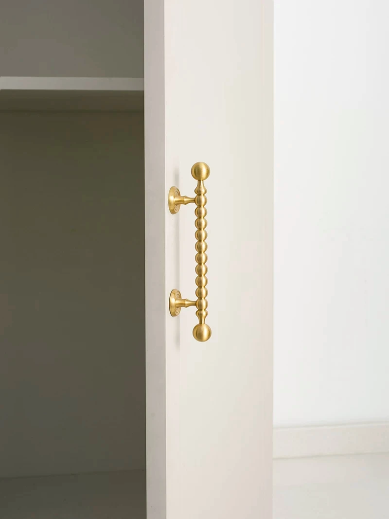 Single beaded brass pull on a white cabinet door