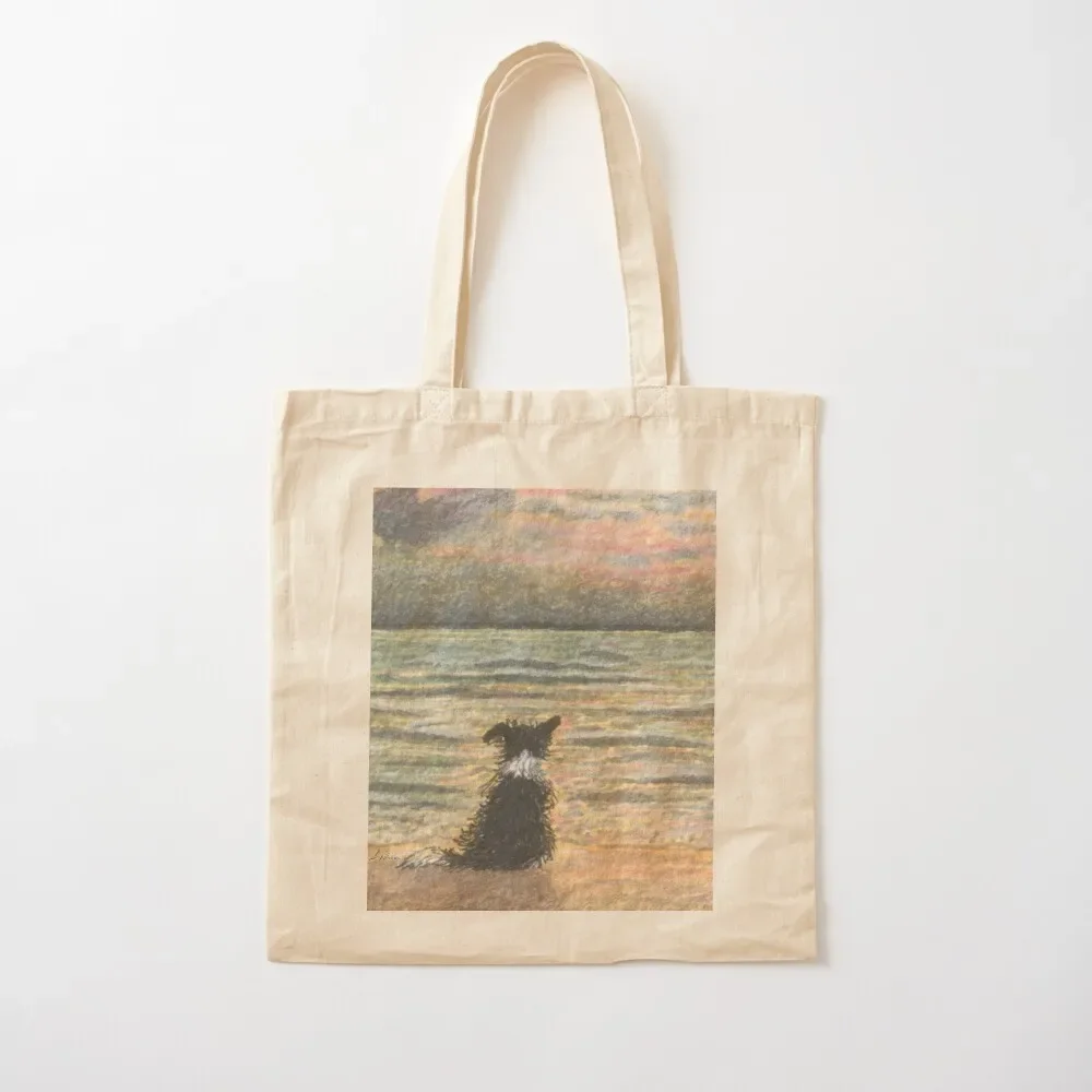 A Border collie dog gazes out over the ocean watching the sun come up, greeting the morning Tote Bag