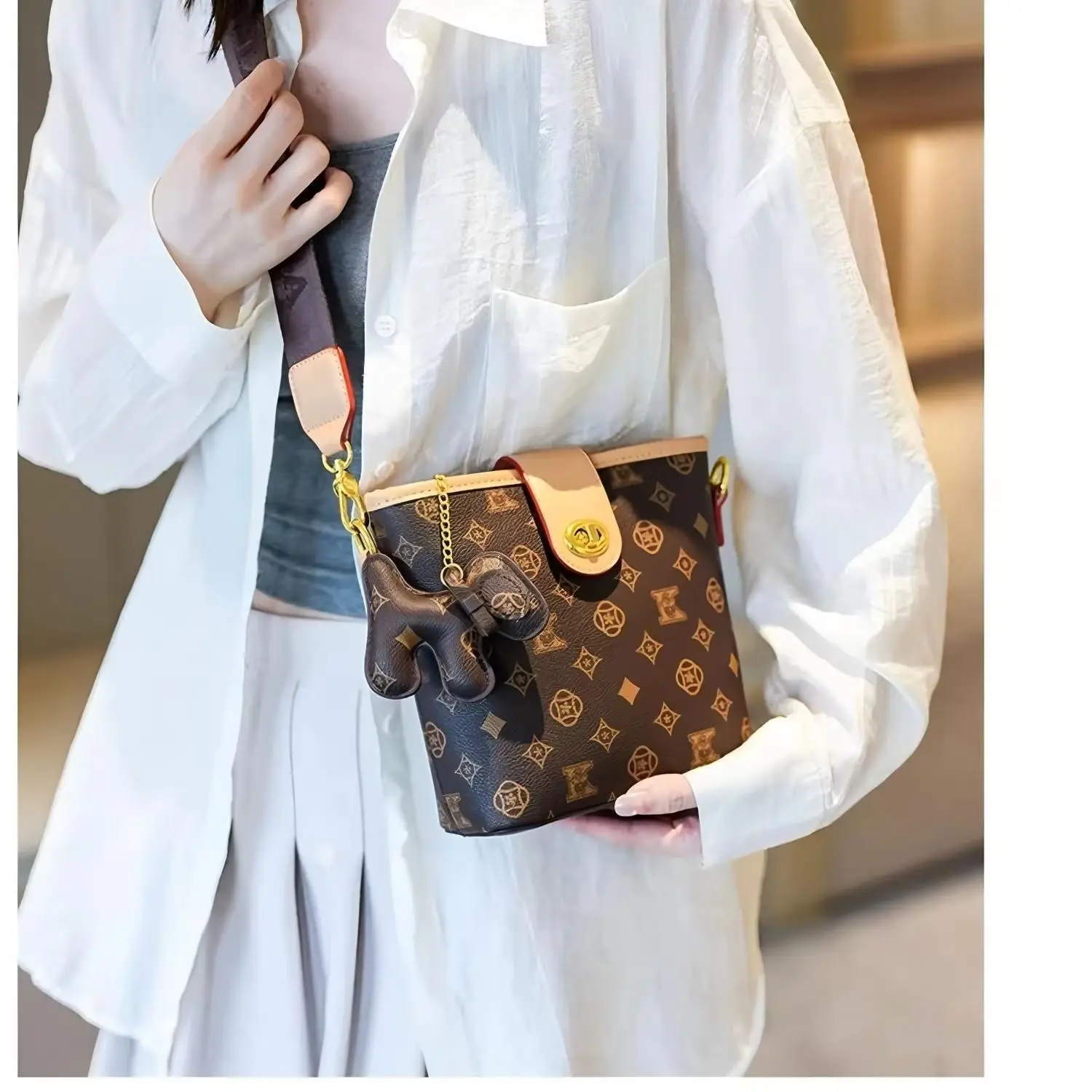 Small brown all-over print bucket handbag with contrasting leather edges and an adjustable wide strap.