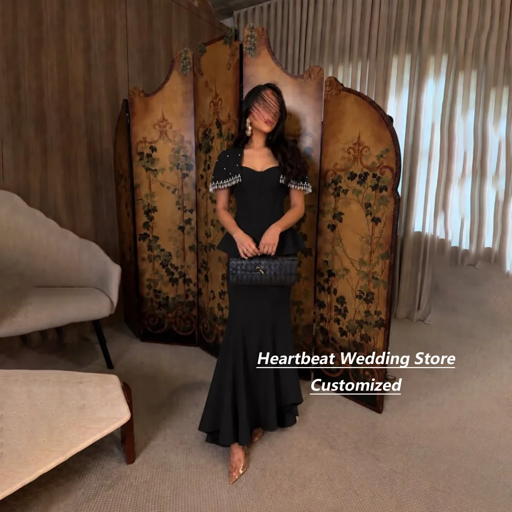 Vestido de noche largo con corte sirena, escote en forma de corazón y detalles de cuentas y flecos, con un gran lazo, ideal para invitadas a bodas y fiestas de graduación, disponible en color negro y con opción de personalización.
