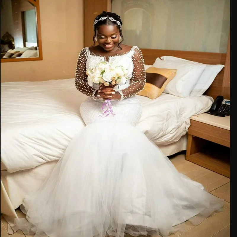 ชุดแต่งงานแบบแอฟริกันสั่งตัดพิเศษ คอเสื้อโปร่งประดับมุกเงางาม พร้อมชายกระโปรงยาวแบบสปีว์เทรน แขนยาวคลาสสิก หรูหรา