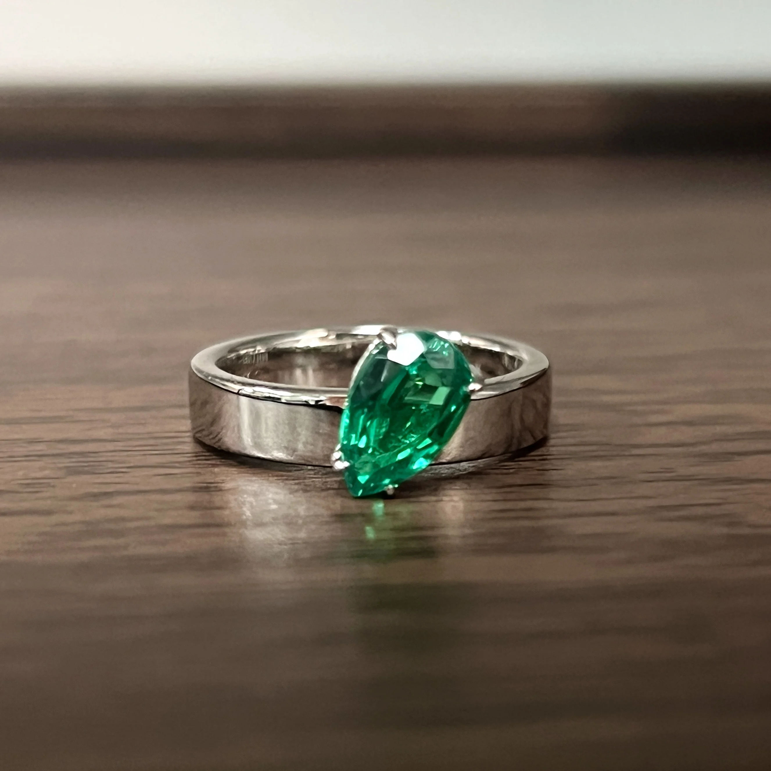 S925 sterling silver drop-shaped ring with 1.5 carats of cultured wood-tone green emeralds. Features wide band design.