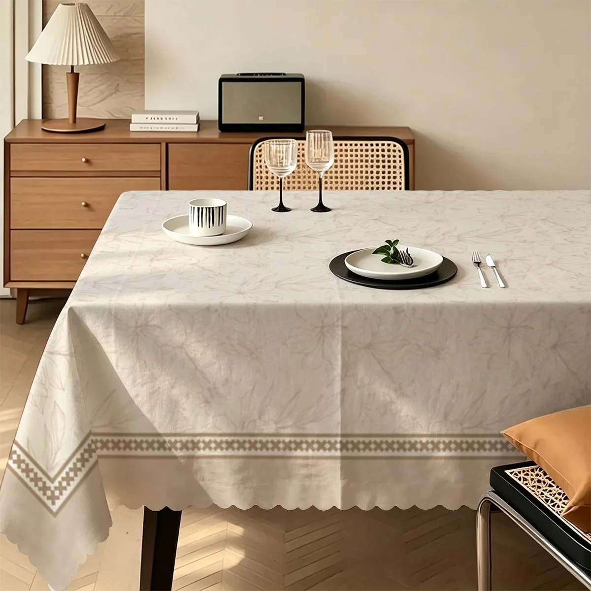 A tablecloth with a pattern featuring light gray fine lines and dark patterns of flower-like designs on a light beige background