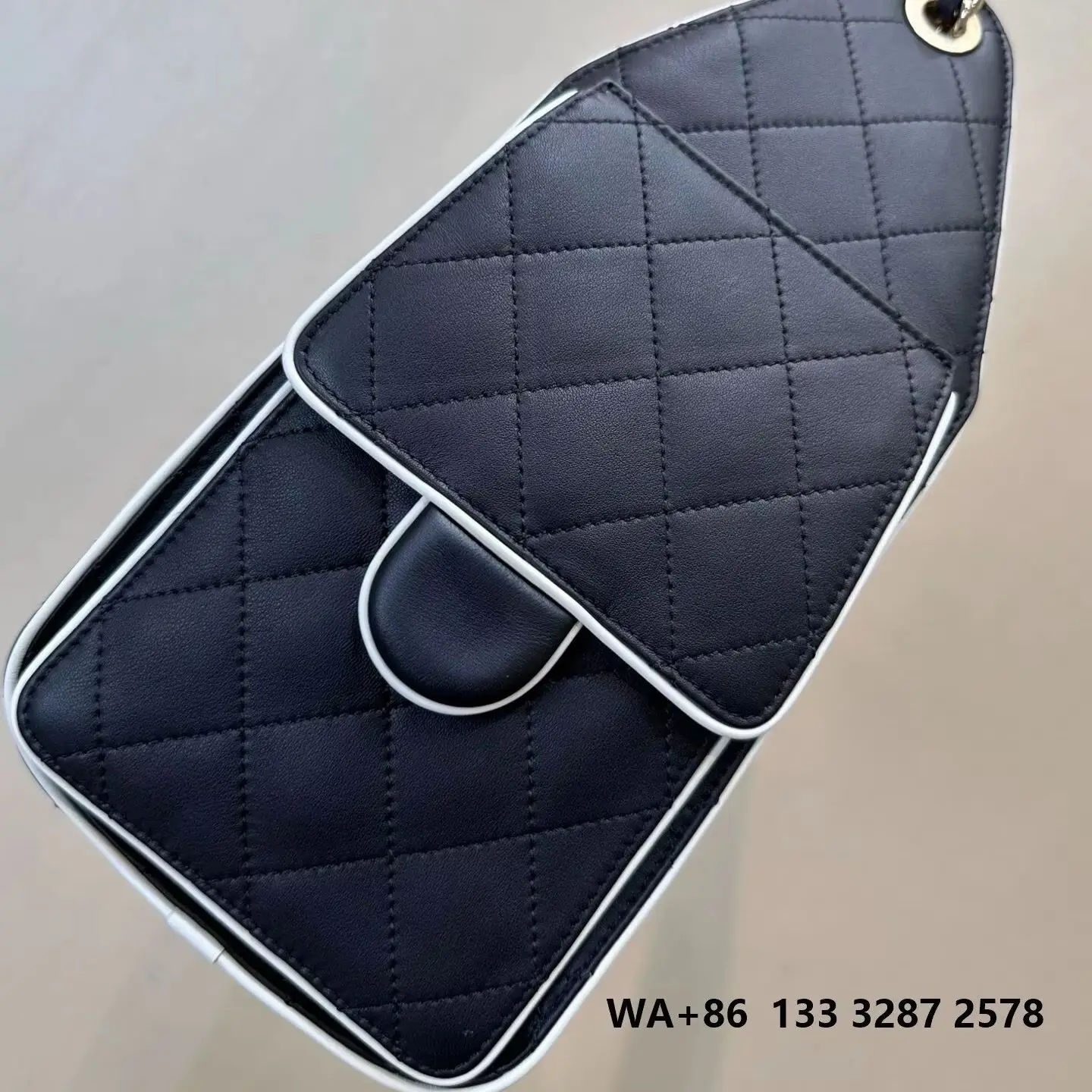 Black leather diamond-quilted drawstring bucket bag, with white-edged trim and woven leather silver chain shoulder strap.