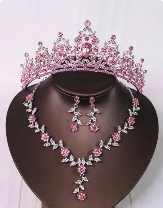 Conjunto de joyería que incluye una corona, un collar y unos pendientes, ambos adornados con cristales rosas, ideal para ocasiones formales, como bodas y fiestas de noche.