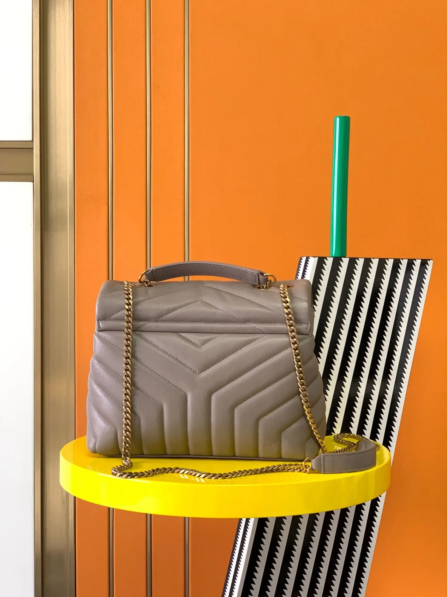 Graue V-förmige Chevron-Handtasche mit gestepptem Klappendesign, doppeltem Tragegriff, Mini-Ledergriffen und dünner Metallkette, aus weichem und flauschigem Leder.