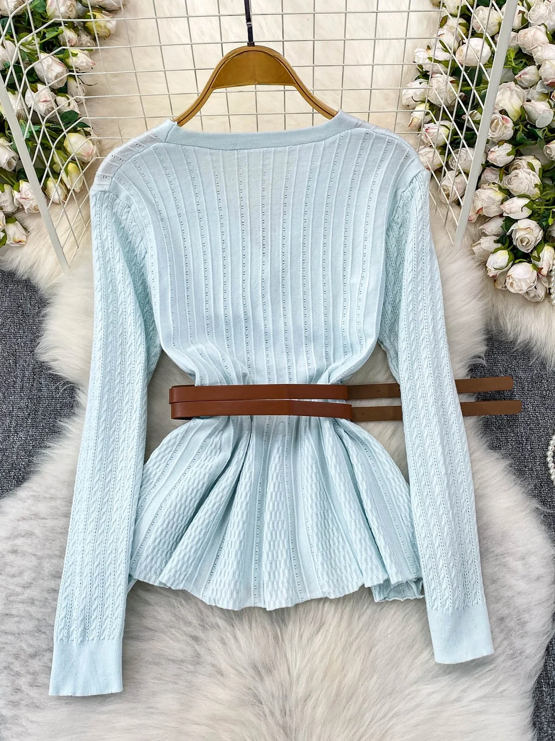 Niebieska dzianinowa bluzka z dekoltem w serek, długim rękawem, ażurowym wzorem, damska, jesienna, elegancka, z paskiem w talii, metalowa, niebieska, delikatny wiatr.