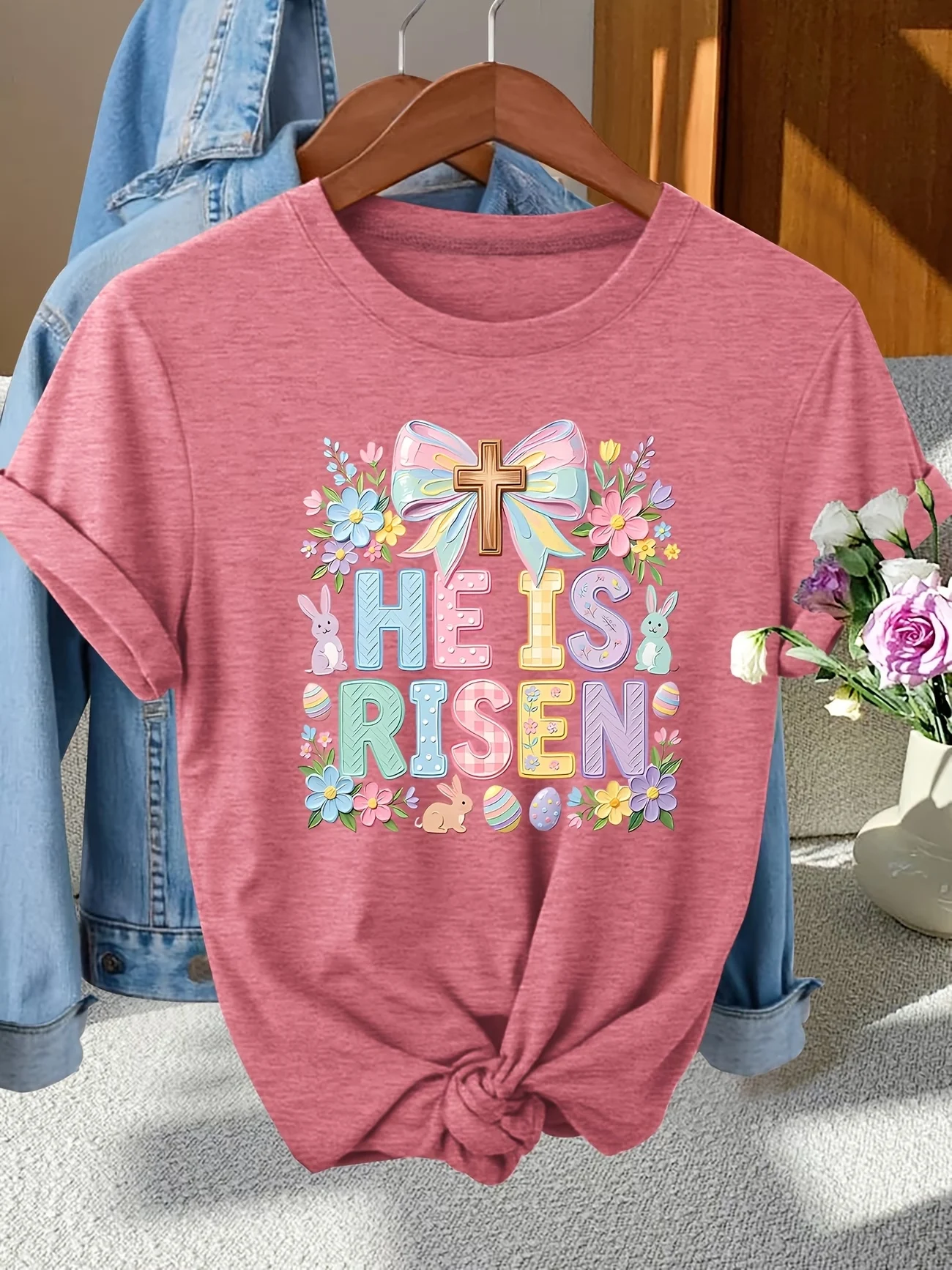 

Featuring a vibrant Easter-themed design with "He is Risen", pastel blooms, bunnies, and eggs, this tee brings a joyful, spiritu