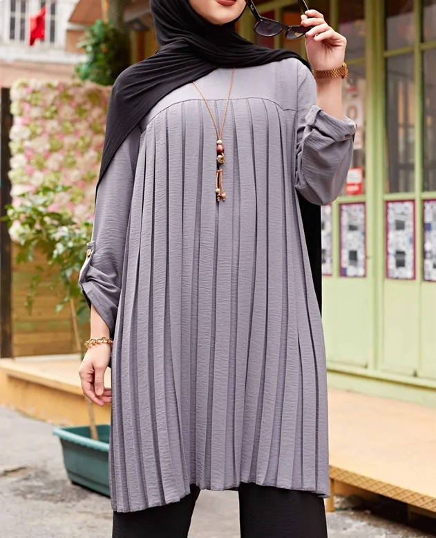 Close front view of gray tunic showing vertical pleats and button-tab sleeves
