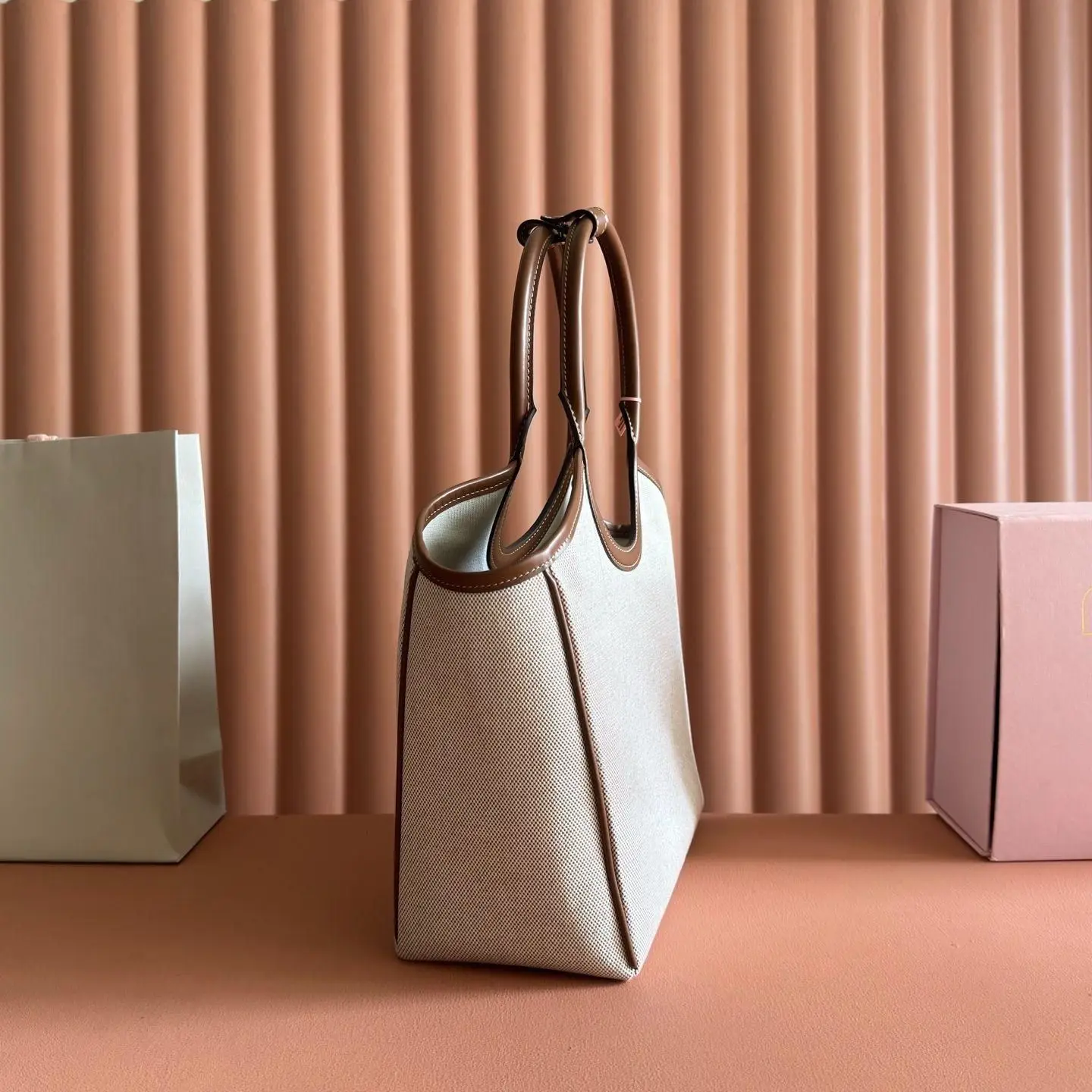 

Light beige canvas handbag with polished brown leather accents, a large circular top handle and clean lines.