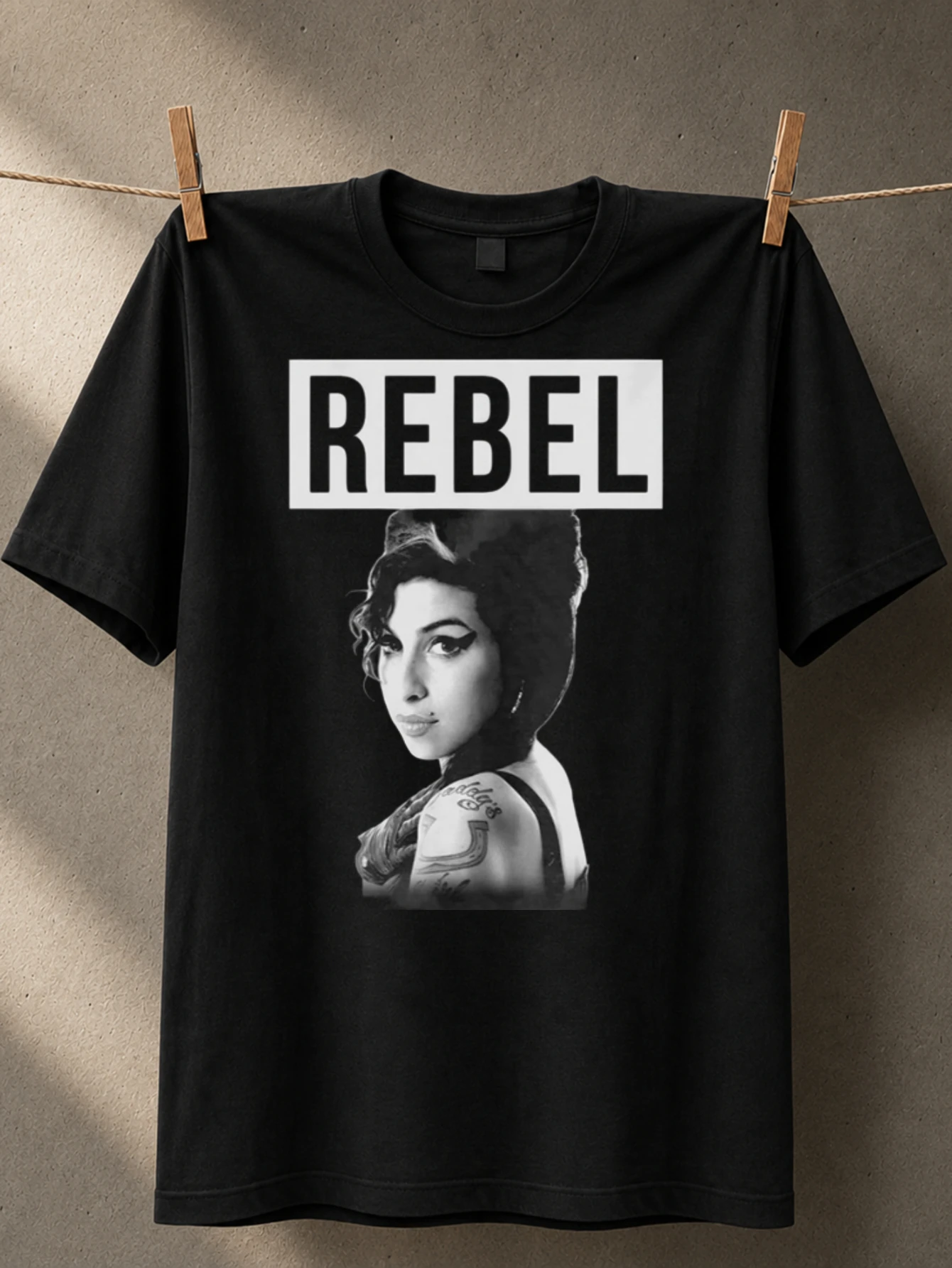 Portrait monochrome d'Amy Winehouse avec inscription Rebel en lettres épaisses et style rétro iconique, T-shirt unisexe.