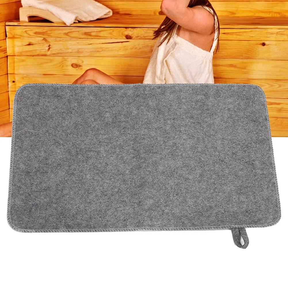 Brown felt oval bath mat with textured surface, placed on a wooden floor near a shower.