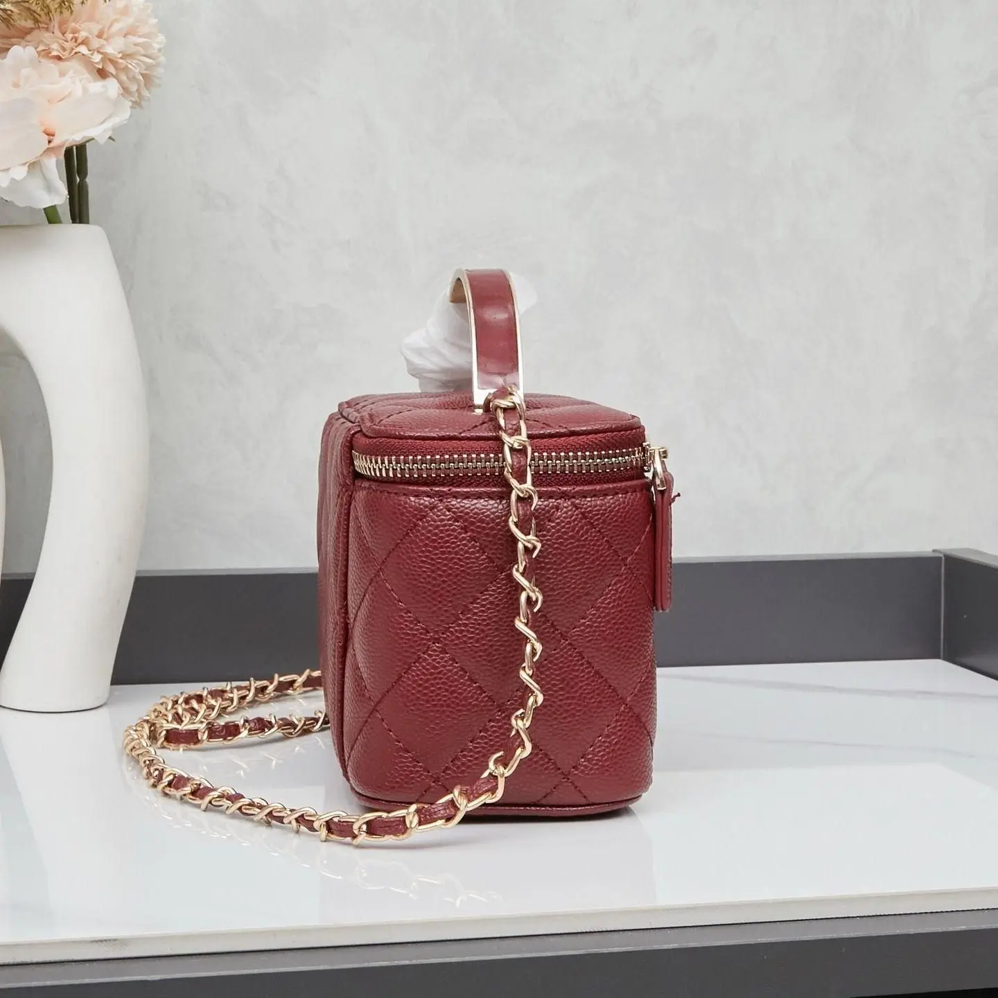 

Diamond-quilted leather mini makeup bag with a pebbled cowhide texture, slim metal top handle, and a double zipper design with leather pull tabs.
