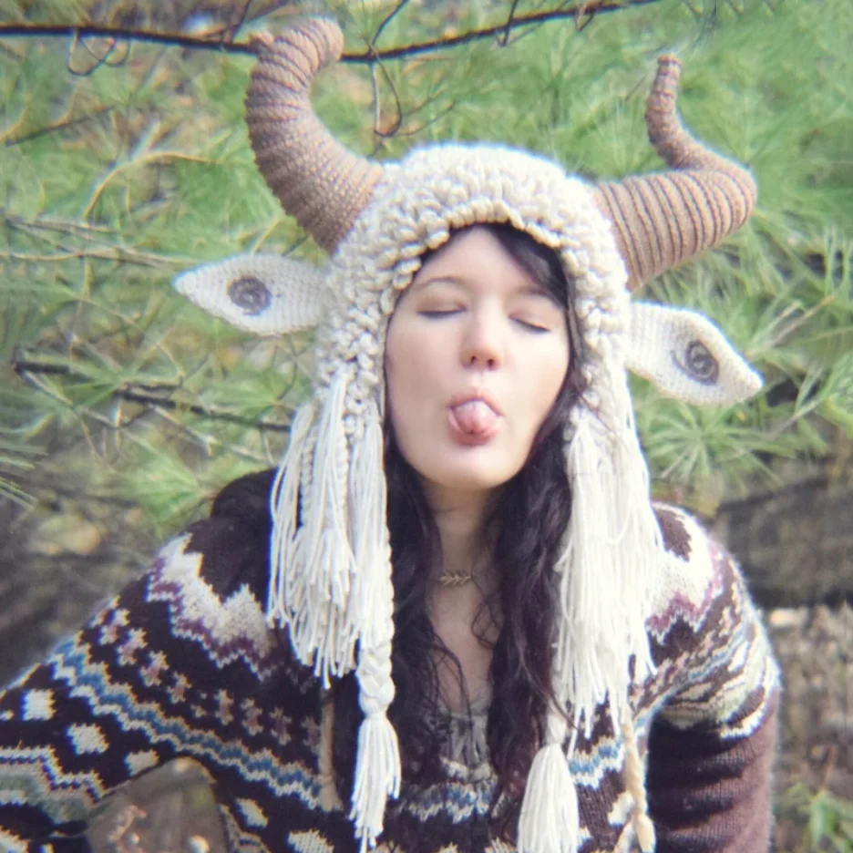 

Hand-Knitted Whimsical Horned Hat with Fringed Ears: A Playful Bohemian Fashion Statement in a Serene Woodland Setting