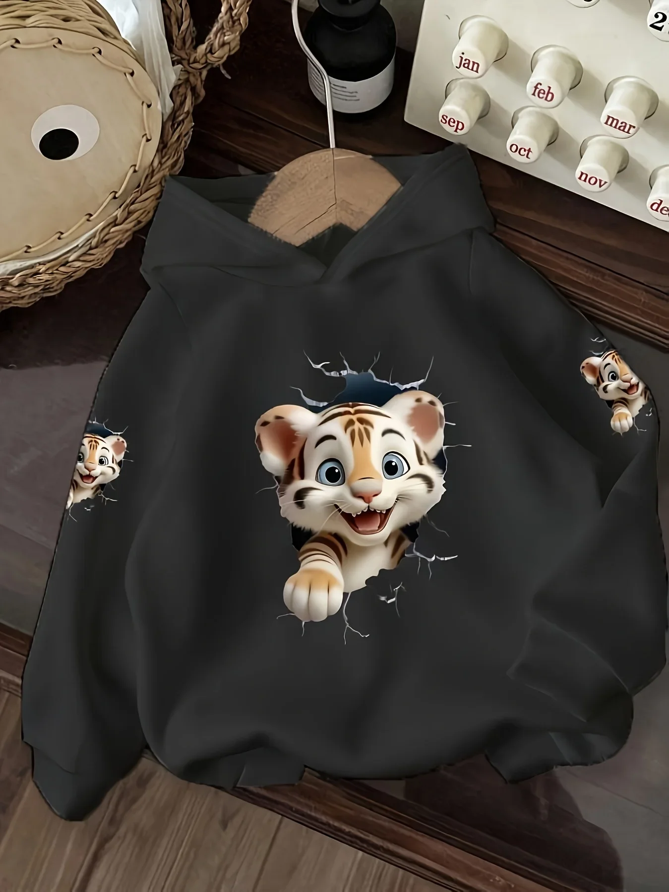 This is a casual hooded sweatshirt forchildren, featuring a cute tiger breaking through awall designIt's a basic everyday style.