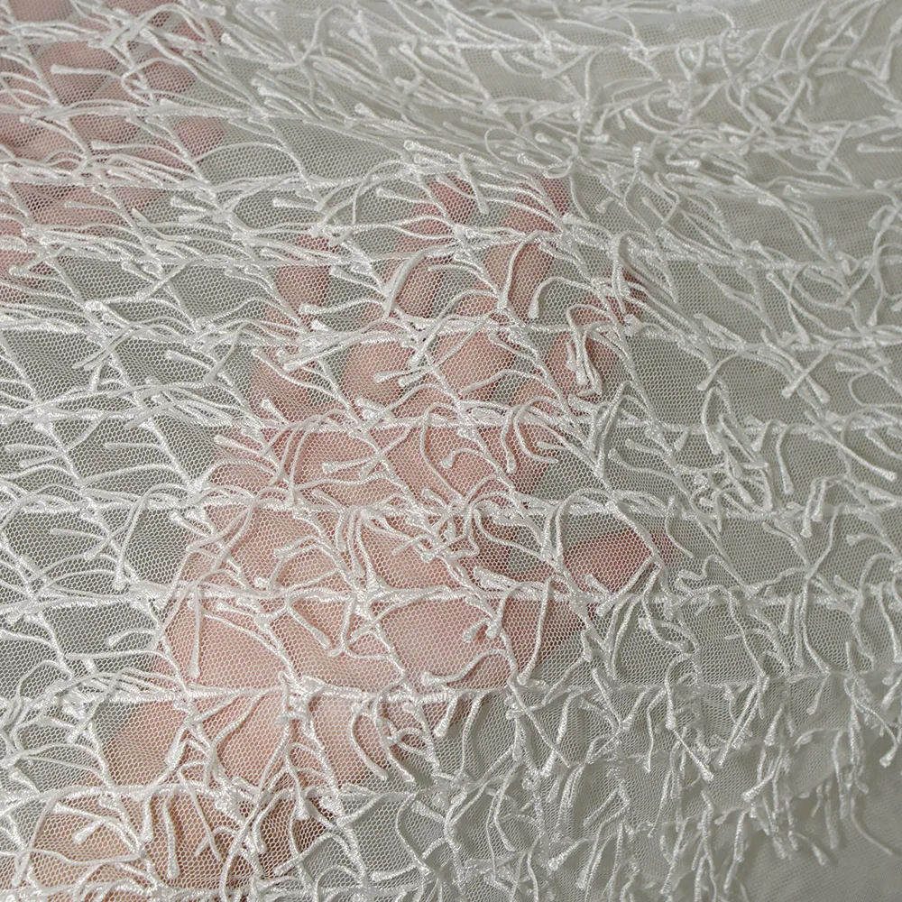 Weißer Spitzenstoff mit Fransen und der strukturierte, netzähnliche Stoff für Hochzeitskleider und formelle Kleider