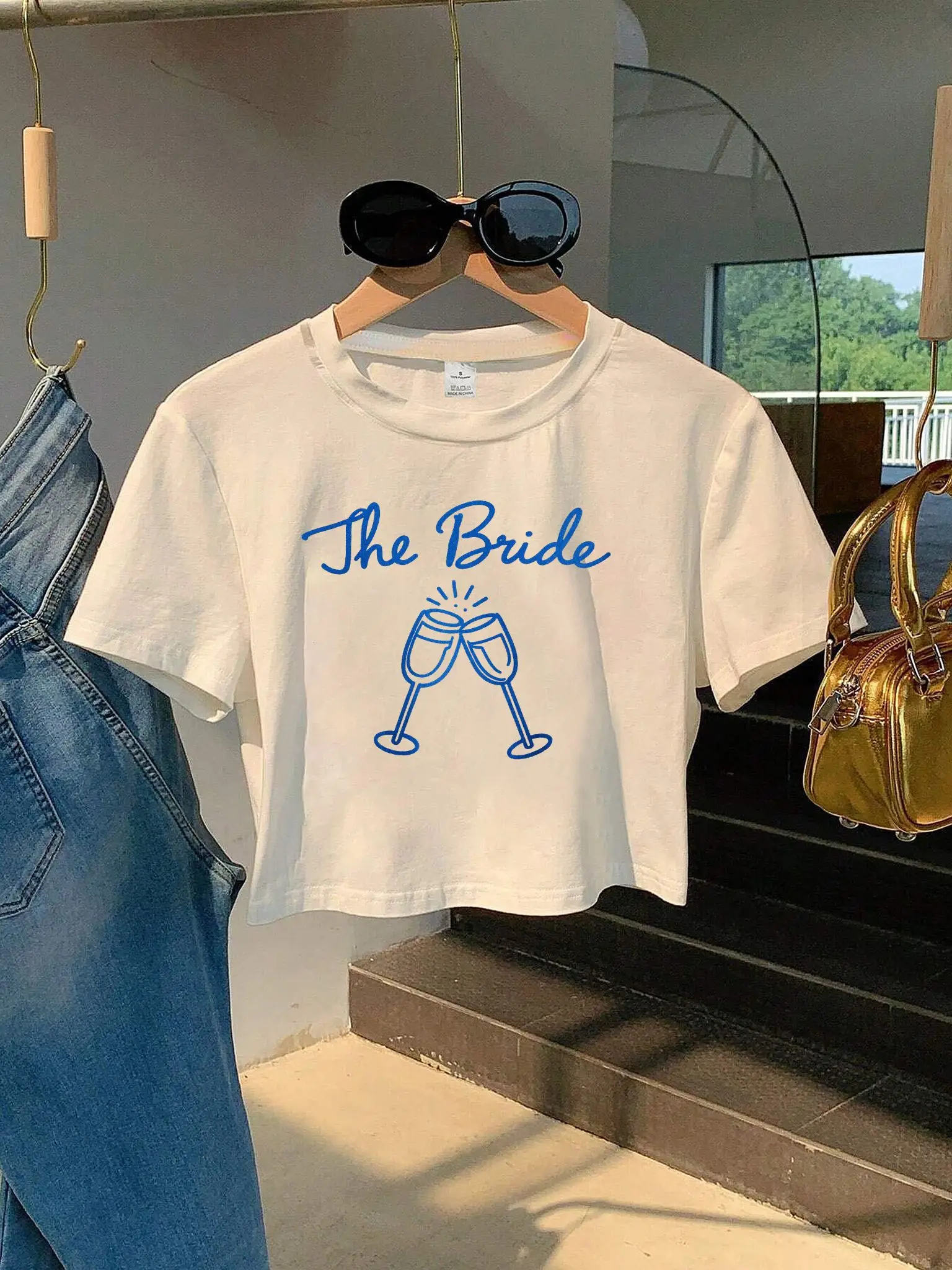 T-shirt court pour femme avec l'illustration 'La Mariée' en texte bleu et flûtes à champagne, col rond, idéal pour les fêtes prénuptiales