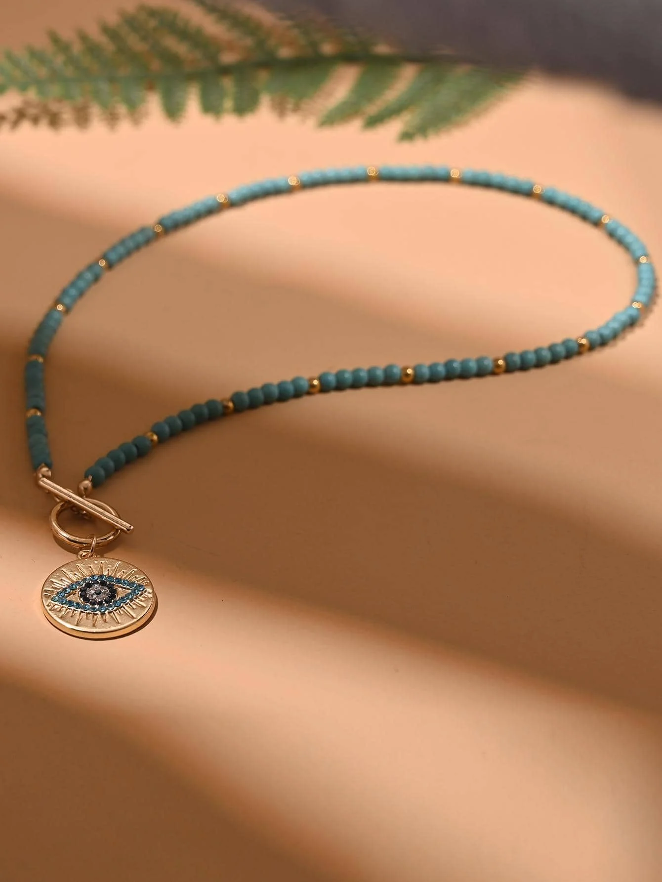 

Ожерелье из бирюзовых бусин с подвеской в виде золотистого оберега от сглаза