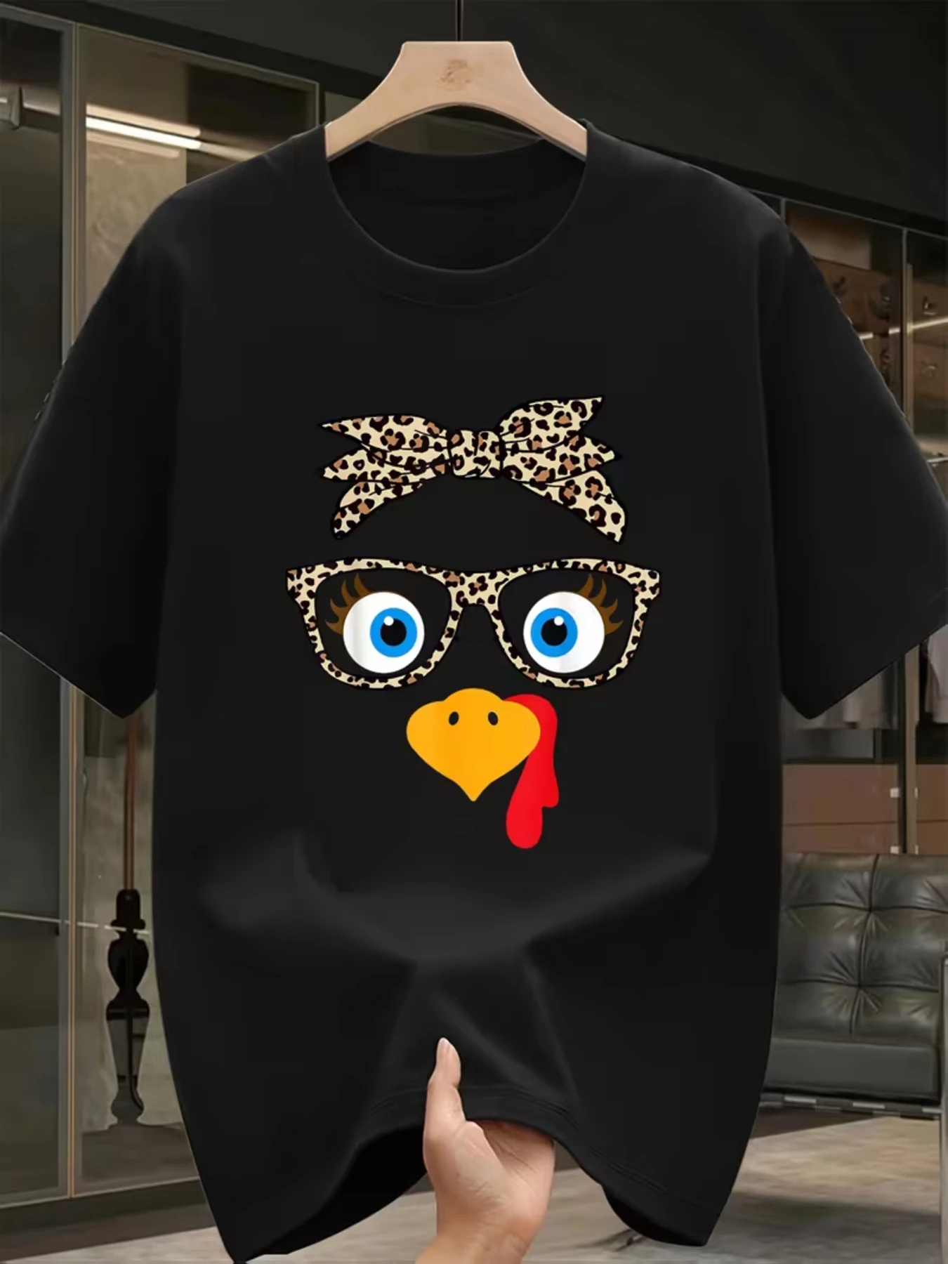 Unisex Black T-Shirt Featuring a Thanksgiving-Themed Leopard Print Design, Complete with a Bow Tie, Glasses, And a Chicken Head Motif with Large Blue Eyes, Long Eyelashes, a Yellow Beak, And a Red Comb. A Modern Minimalist Gift for The Holiday