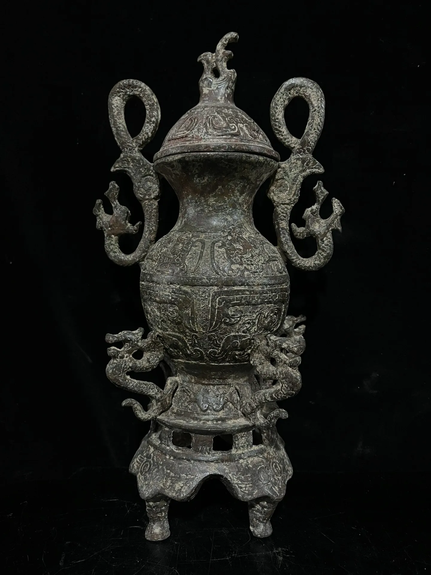 Old bronze vessel featuring red and green patina, adorned with twin dragon motifs.