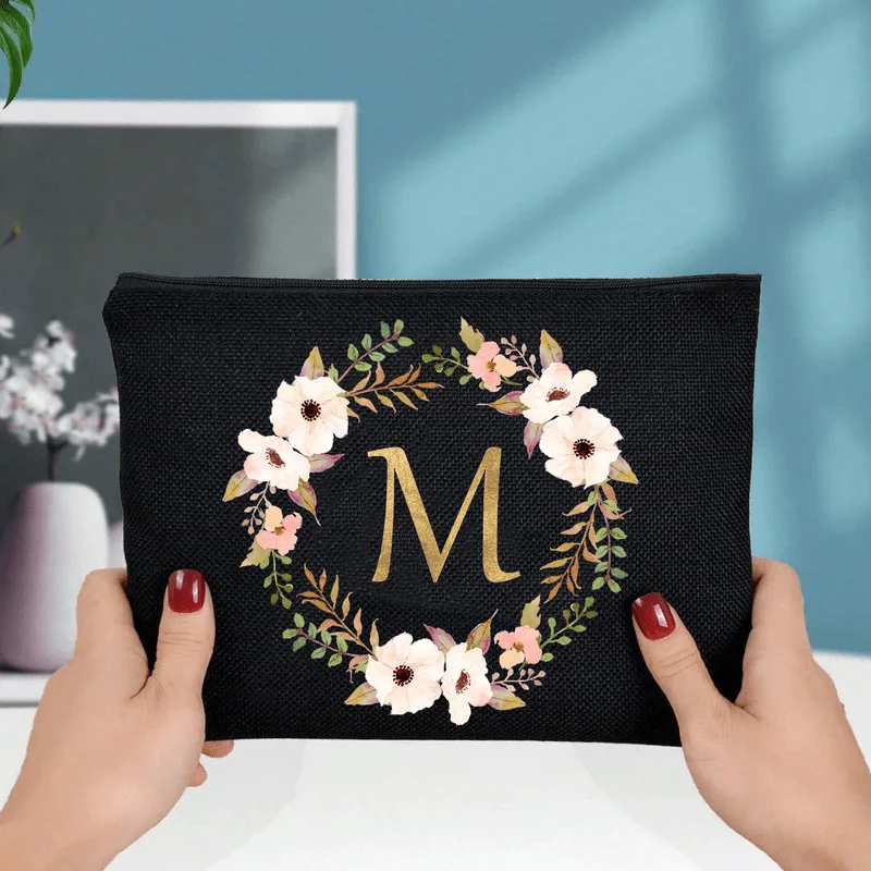 An Elegant Floral Makeup Bag Featuring A Golden 'M' Letter - Designed With Black And Beige Flowers This Lightweight And Durable