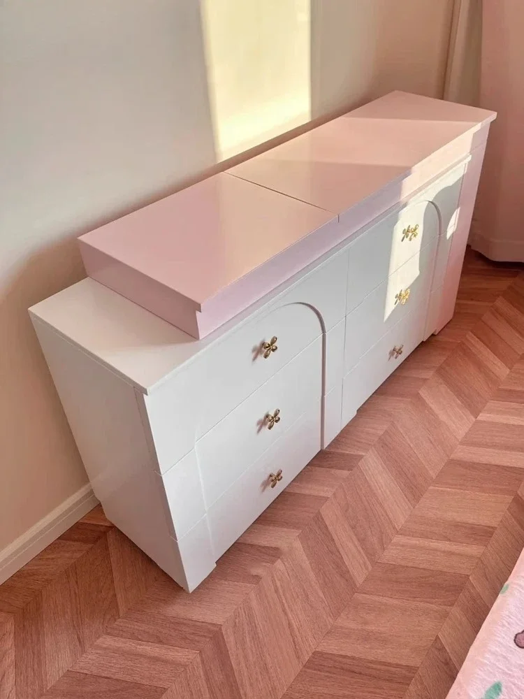 

Розовый комод-тумба с шестью ящиками и встроенным шкафом для хранения.