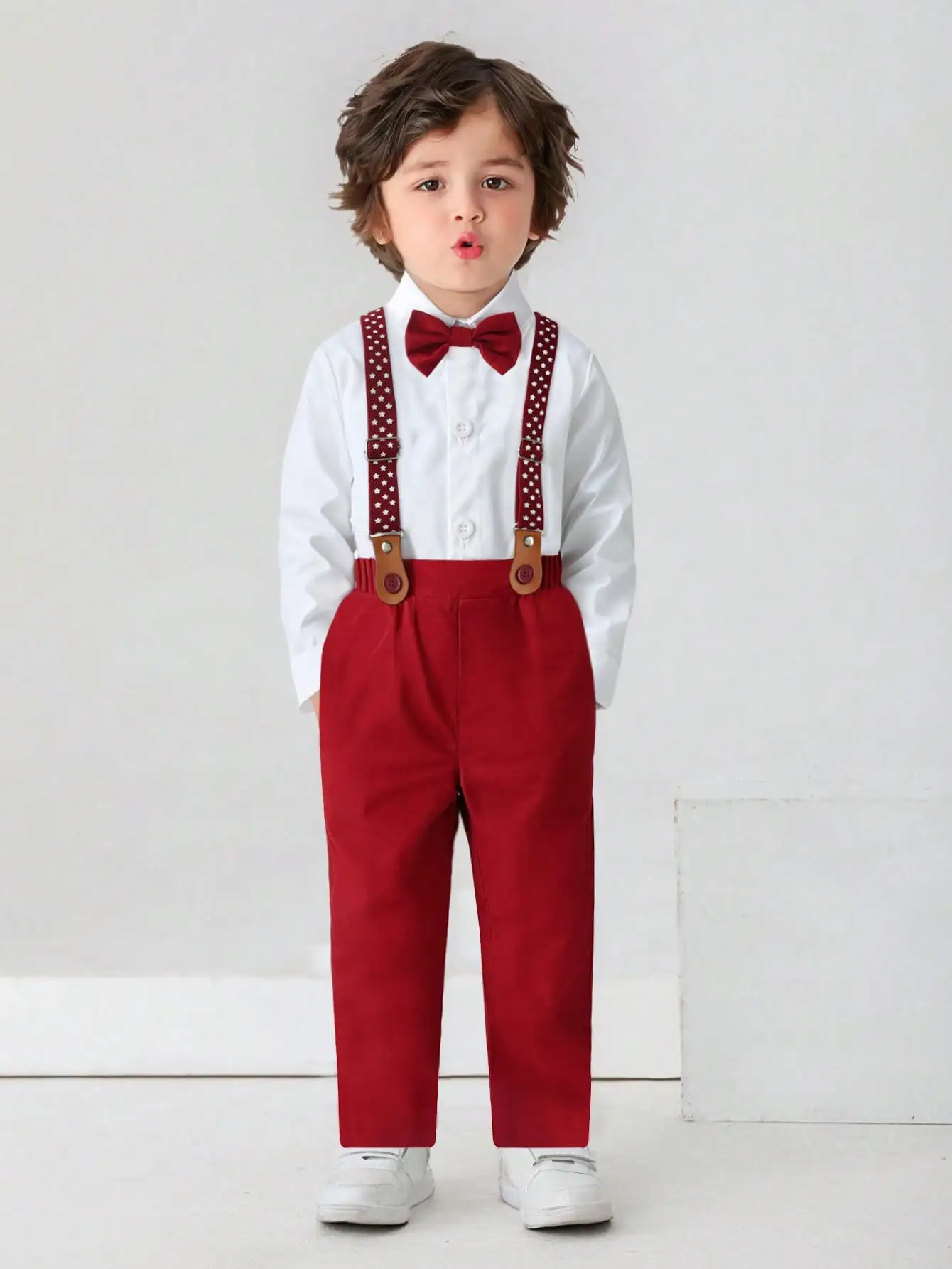 

Нарядный костюм для мальчиков: белая рубашка с длинным рукавом, красный галстук-бабочка, подтяжки со звездным принтом и красные брюки.