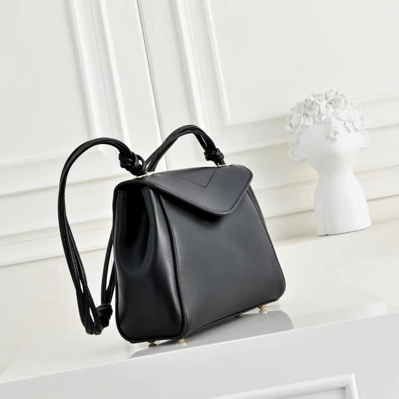 Pure black smooth leather flap crossbody bag with a V-shaped cut on the front flap, multiple leather strap knots, and anti-scratch metal studs on the bottom.