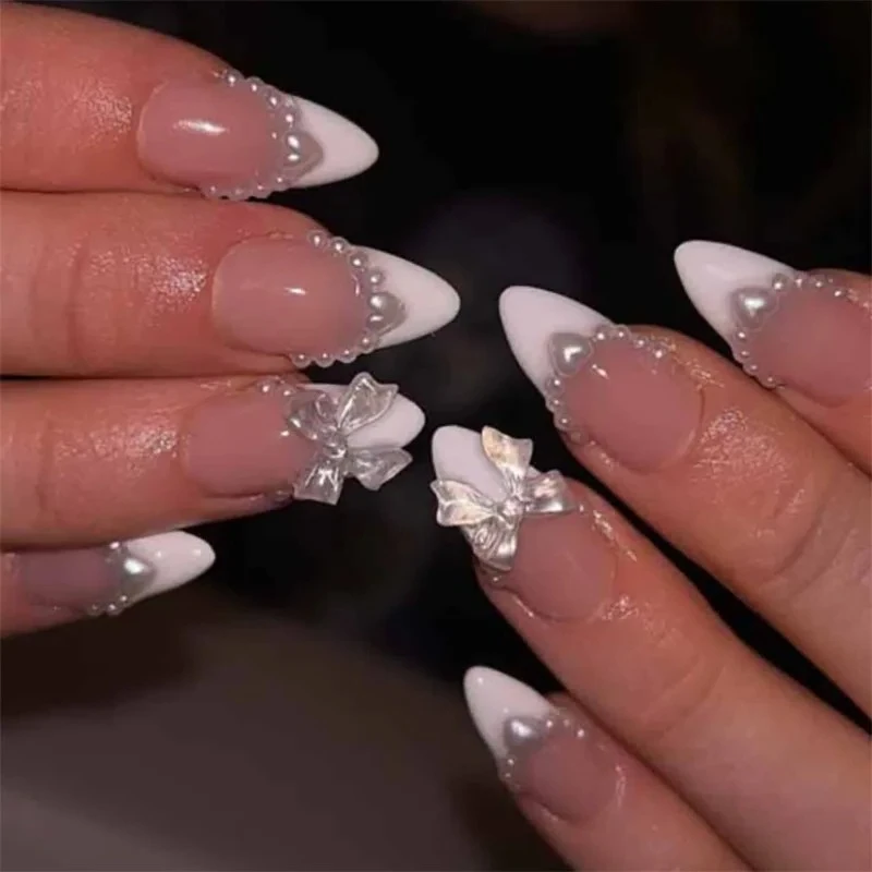 ピンクホワイトのリボン結び、キラキラ光るラインストーン、フレンチパール、ヌードアーモンド型の付け爪、ミディアムポインテッドのつけ爪、プレスオンネイル、マニキュア